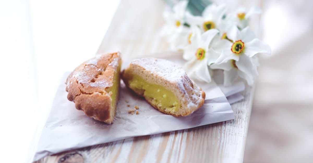 A half-eaten lemon tart on a rustic wooden table, with daffodils in the background.