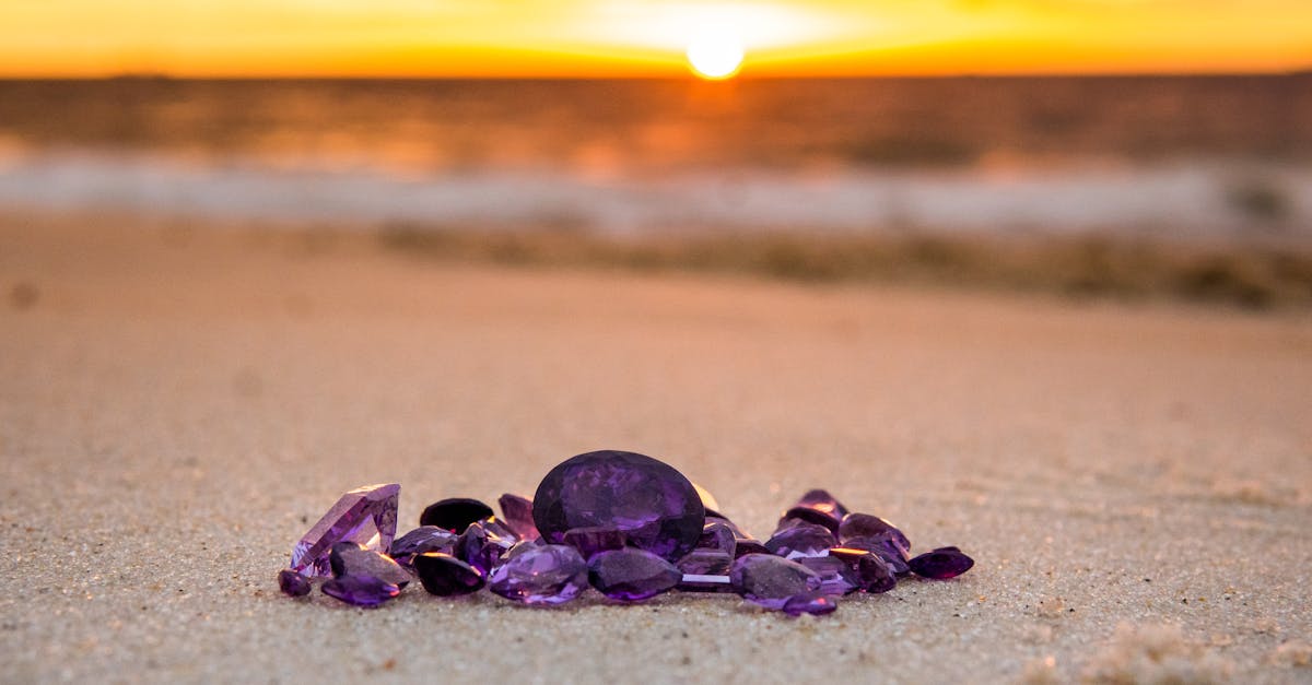 A collection of amethyst gemstones glistens on a sandy beach at sunset.