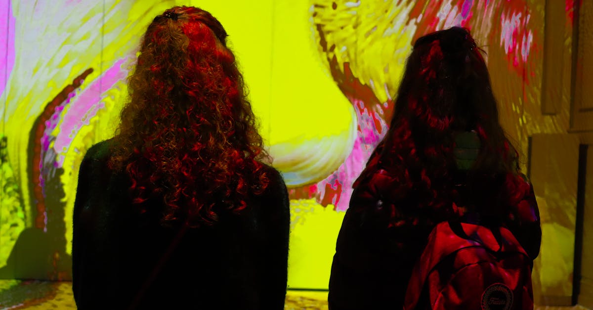 Two women with backpacks viewing vibrant digital art in a museum setting.
