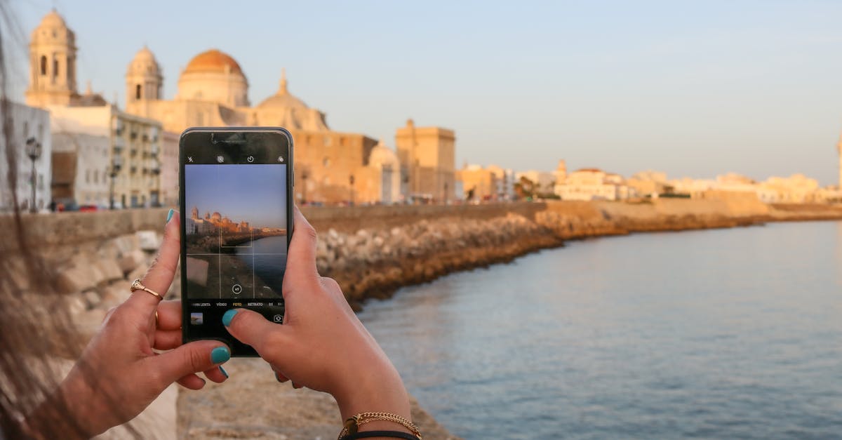 Woman photographing beautiful Cadiz waterfront scene with smartphone during golden hour.