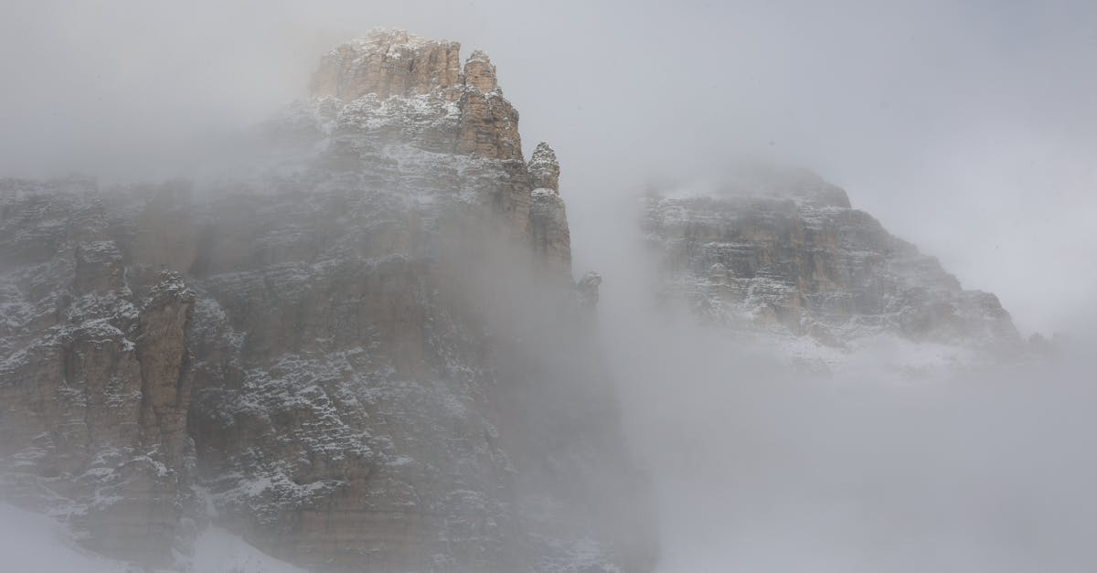 Dramatic mountain landscape with snow-covered peaks emerging from dense fog, highlighting nature's majesty.