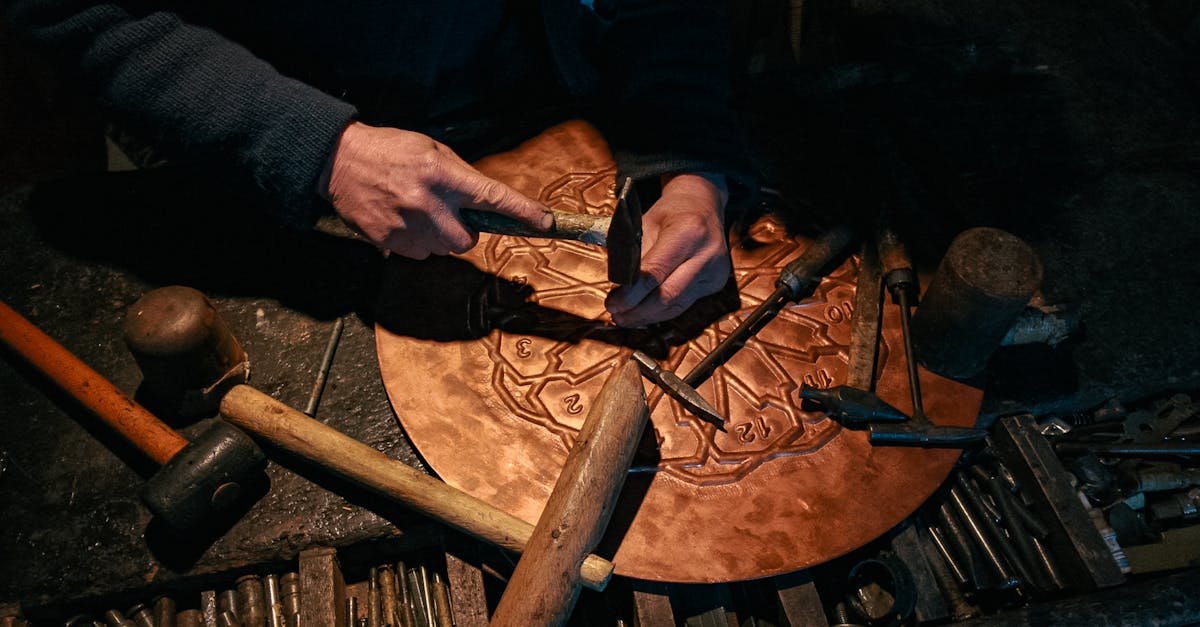 An artisan meticulously crafting a detailed metal plate using traditional tools in a dimly lit workshop.