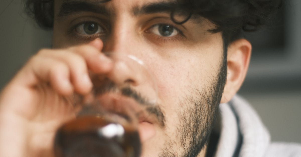 Close-up of a bearded man sipping a drink indoors with focus on eyes.