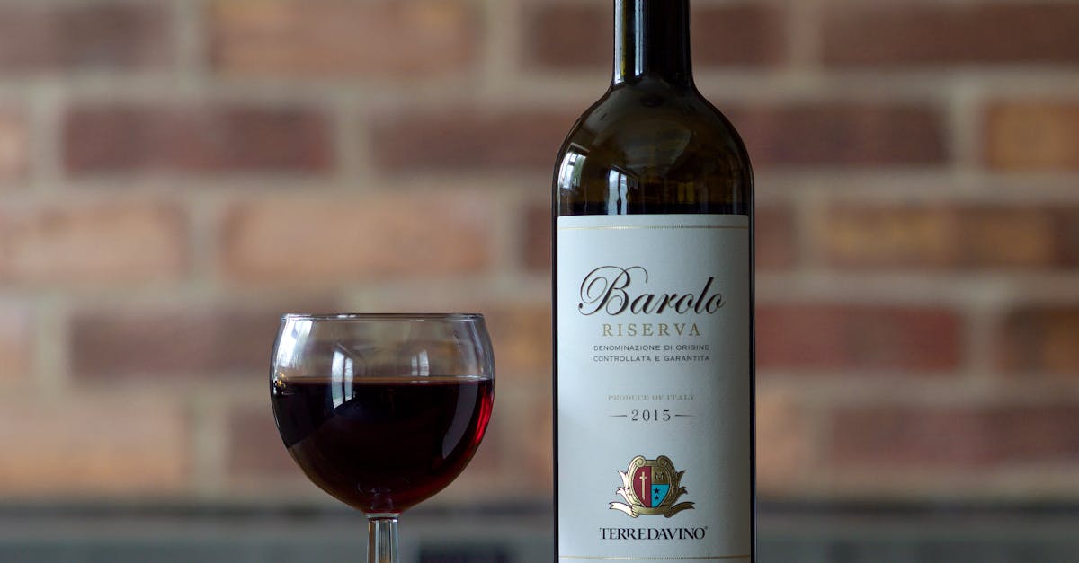 Barolo Riserva 2015 bottle with wine glass on a wooden table against a brick wall.