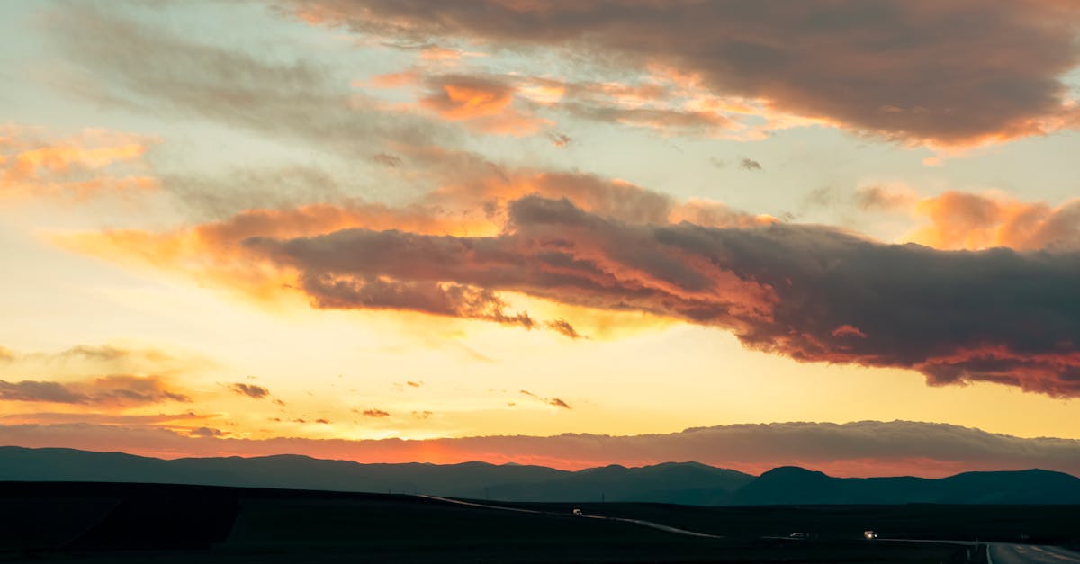 Breathtaking view of a sunset over mountains with vibrant clouds and a winding road.