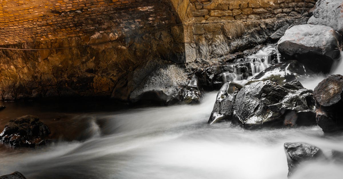 A serene long exposure shot of a stream flowing under a stone arch bridge, capturing the beauty of nature.