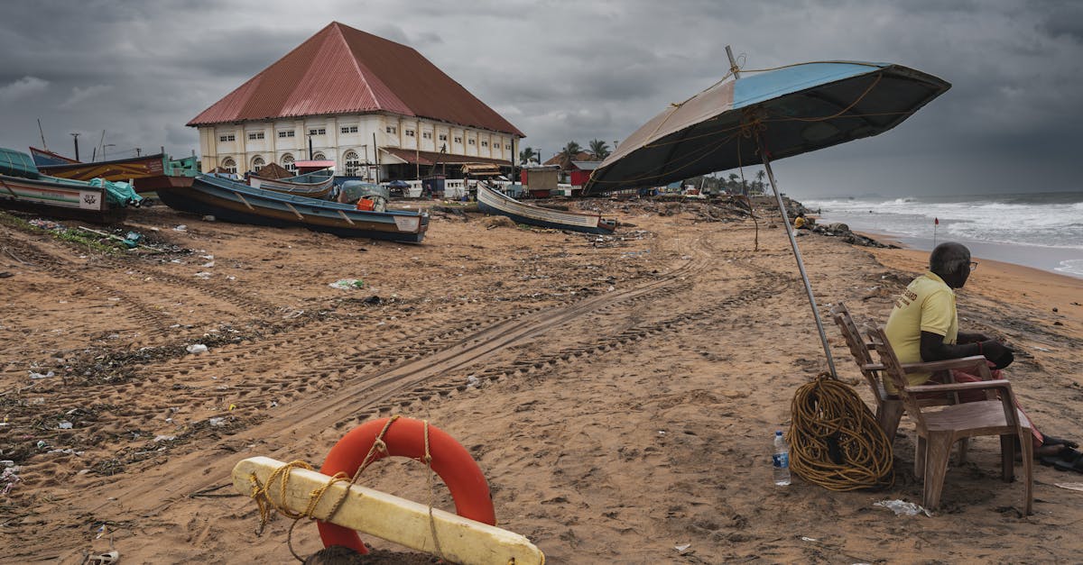 Stormy beach scene with boats, lifeguard, and large building under dark clouds, conveying a moody coastal atmosphere.