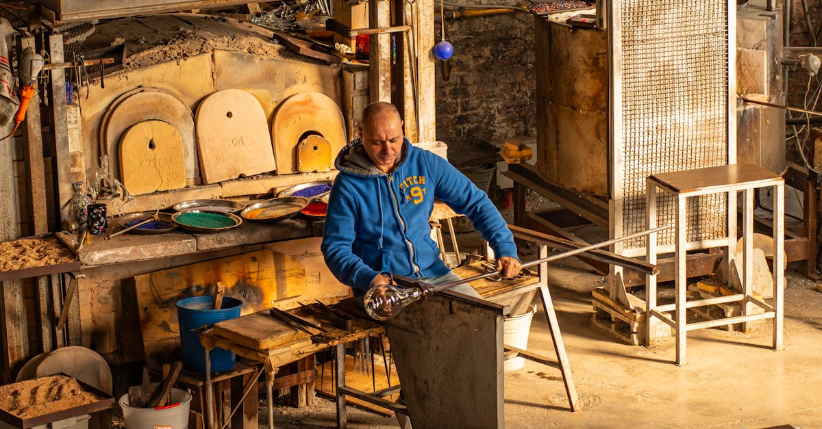 Glassblower crafting art in traditional Venetian workshop with furnaces and tools.
