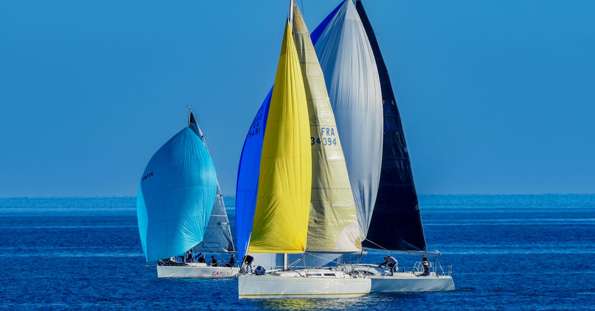 Three vibrant sailboats competing in a sailing race on the open sea under a clear blue sky.