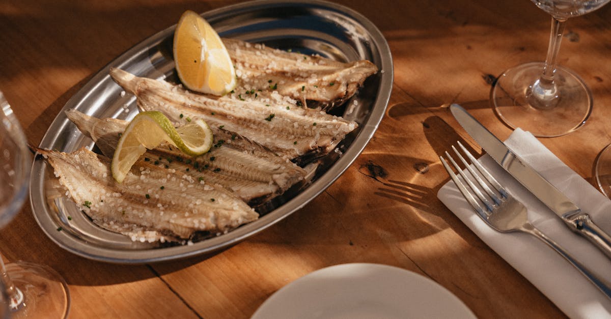 A platter of grilled fish garnished with lemon slices on a sunny outdoor dining table.