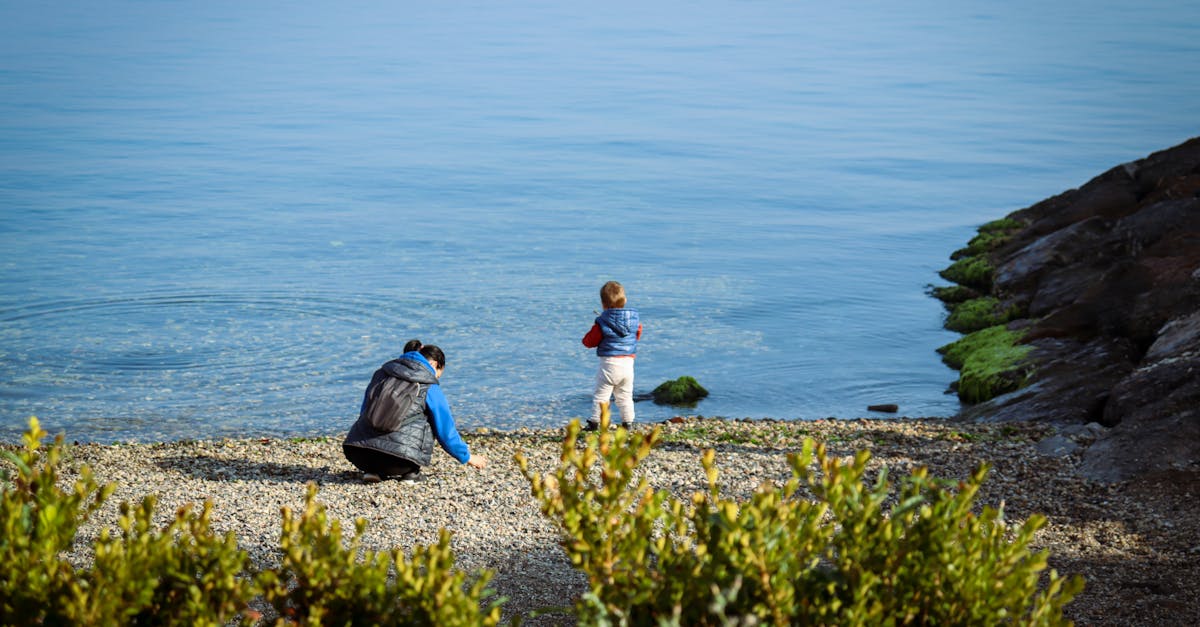 A parent and child enjoy a serene moment by the calm lakeside with clear water.