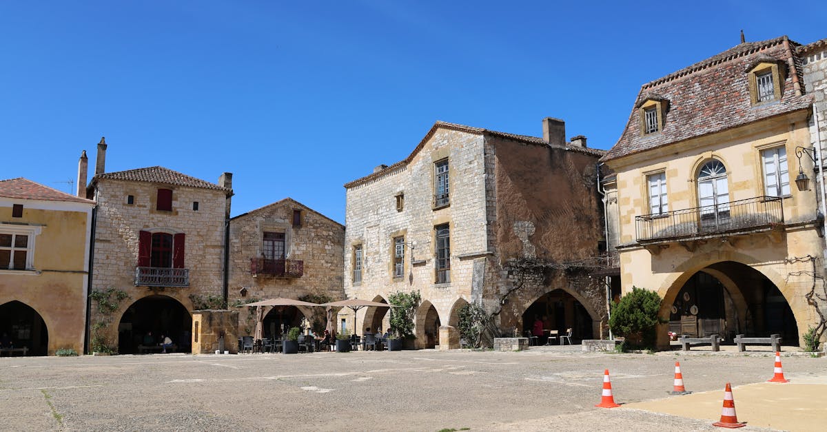 Charming stone buildings lining a sunlit plaza in a historic French village.