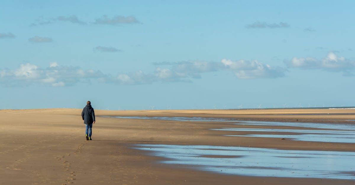 Solitary figure walking along a deserted beach with expansive sky and sea views.