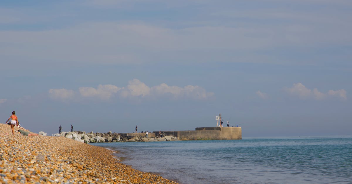 Peaceful pebble beach with people enjoying a sunny day by the pier.