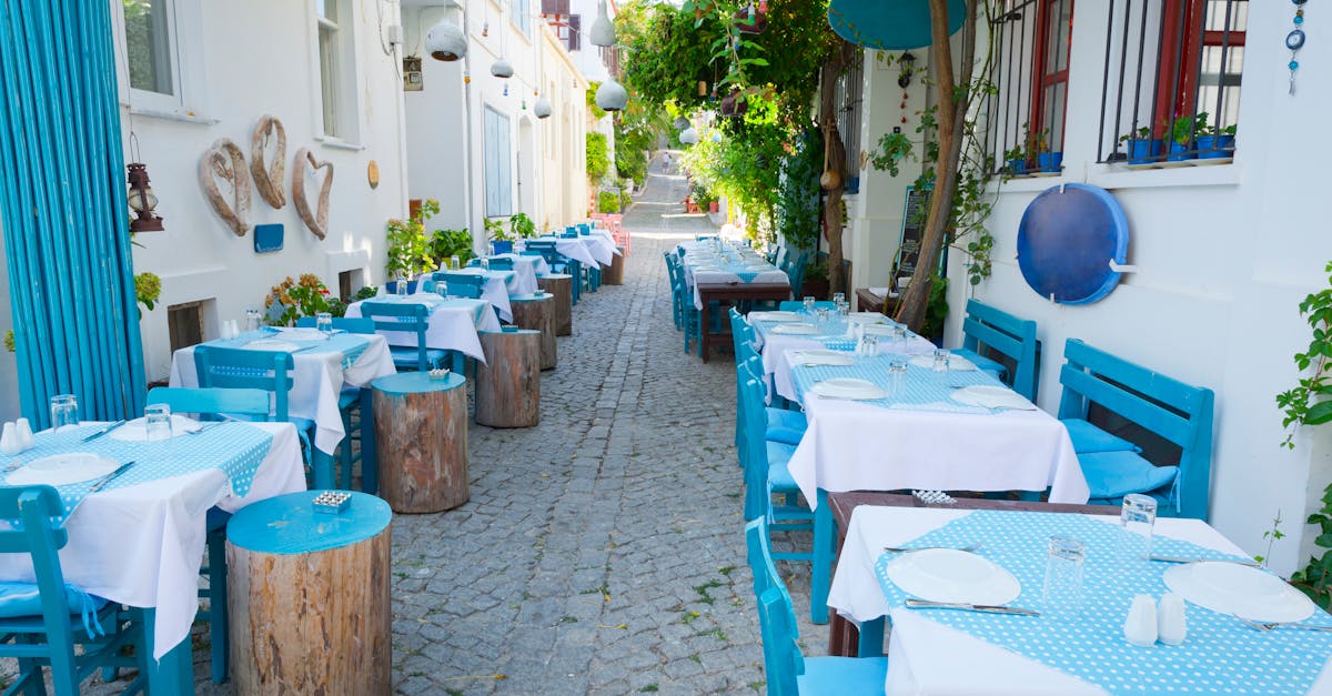 A vibrant, empty Mediterranean street restaurant with blue decor and cobblestone path in Bozcaada, Turkey.