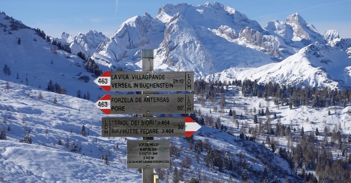 Snowy mountains and trail signs in the Dolomites under clear blue skies.