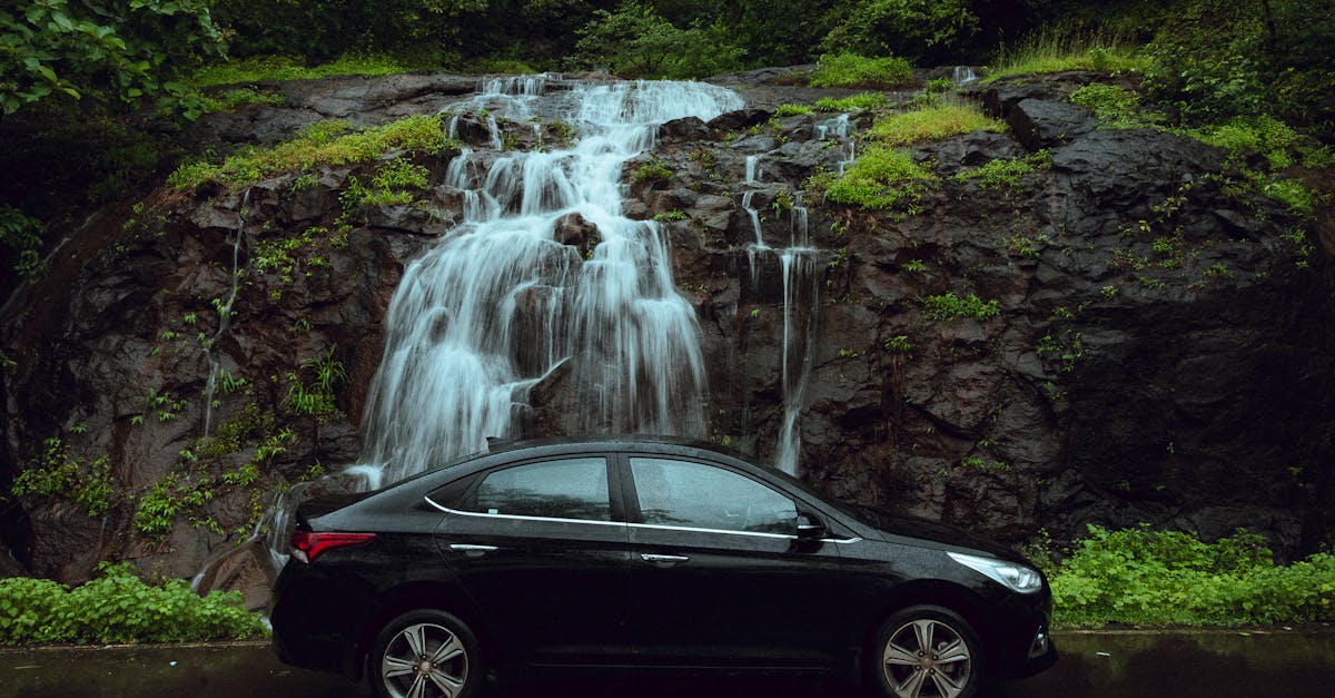 Black car parked in front of a serene waterfall surrounded by greenery in Mumbai, India.