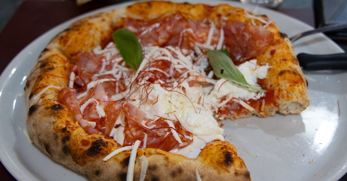 A mouth-watering Italian pizza topped with prosciutto, cheese, and basil leaves on a white plate.