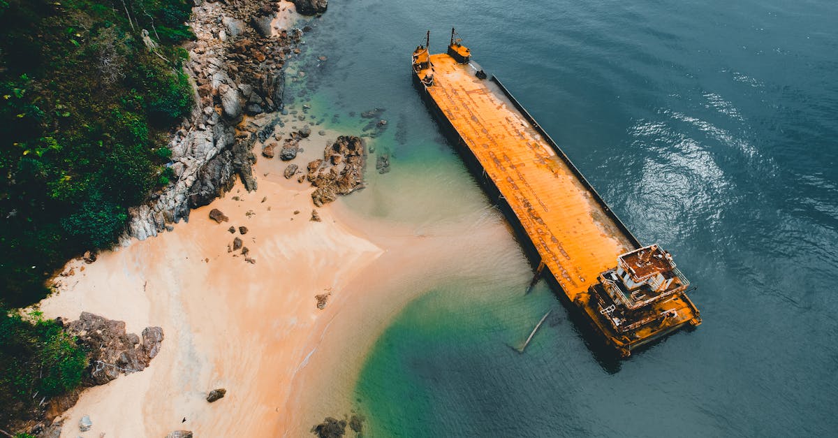 Drone shot of an abandoned shipwreck on a remote sandy beach, surrounded by rocky cliffs and turquoise waters.