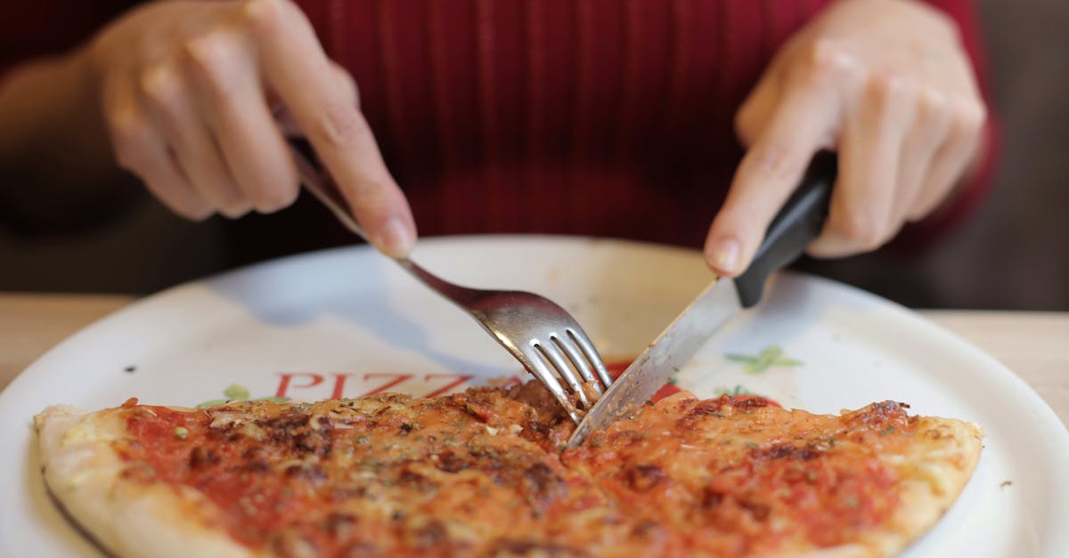 Close-up of hands slicing a delicious cheese pizza with fork and knife.