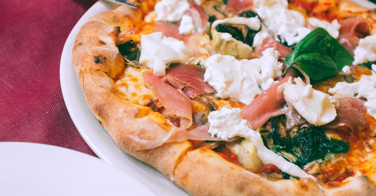From above of appetizing homemade pizza with prosciutto mozzarella and spinach served on plate and placed on table in cafe