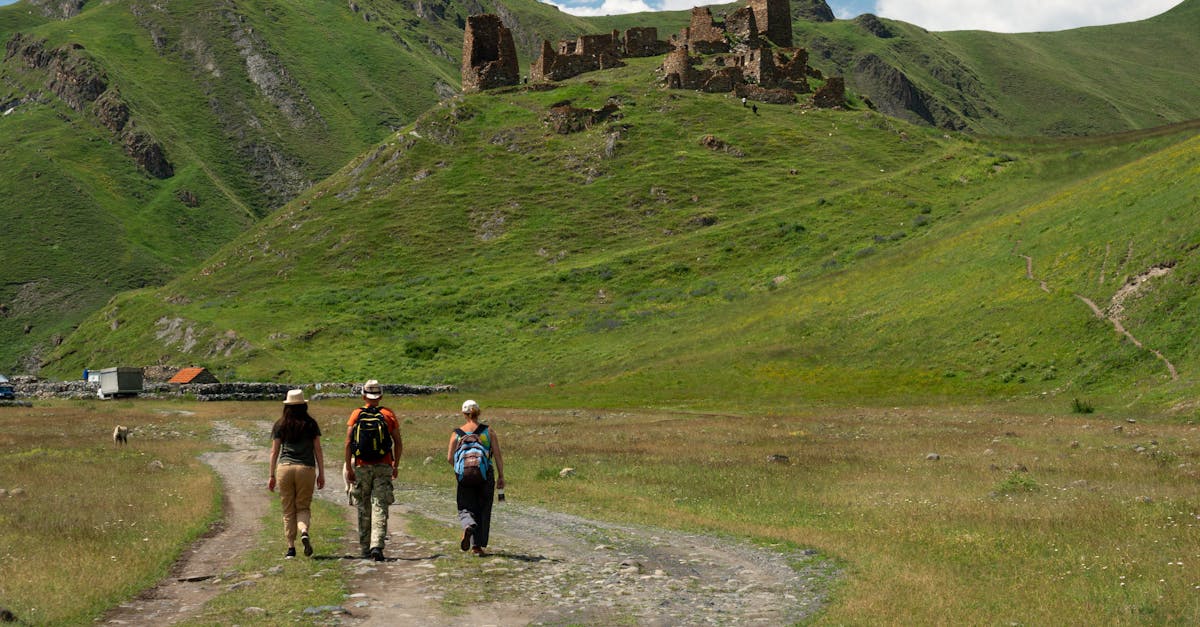 Three hikers walk towards ancient ruins in the scenic mountains of Mtskheta-Mtianeti, Georgia.
