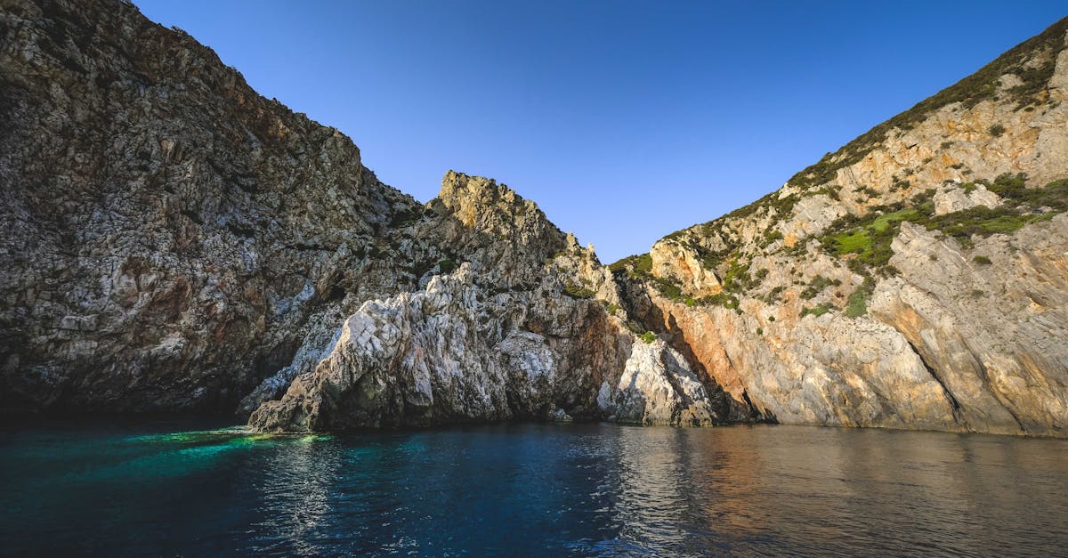 Colorful turquoise lagoon next to tall steep cliffs covered with grass and bushes under vibrant blue cloudless sky