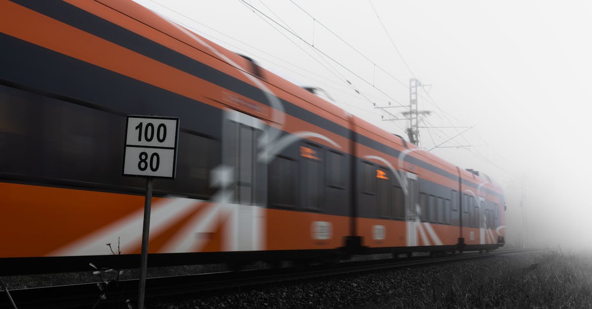 Orange train speeding on railway tracks in dense fog with speed sign visible.