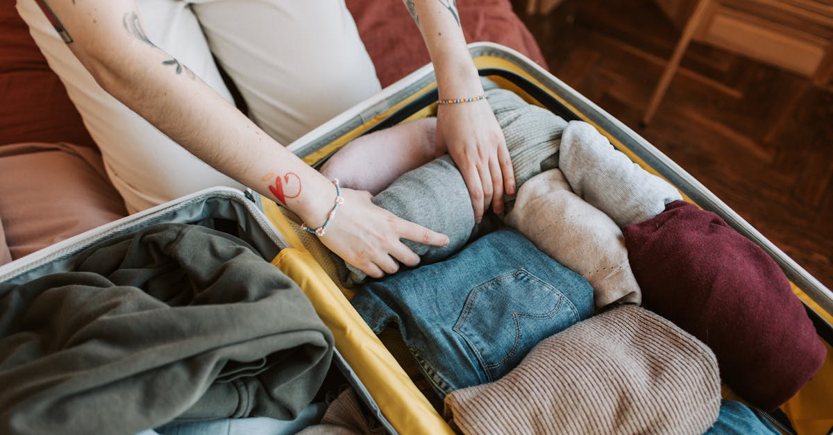 Close-up of a person packing various clothing items into a suitcase, ready for travel.