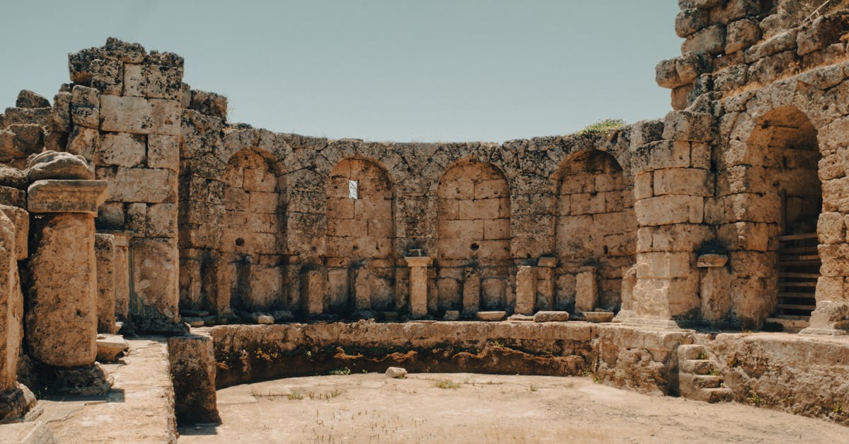 Ancient stone ruins feature historic arches and rugged landscape under clear sky.