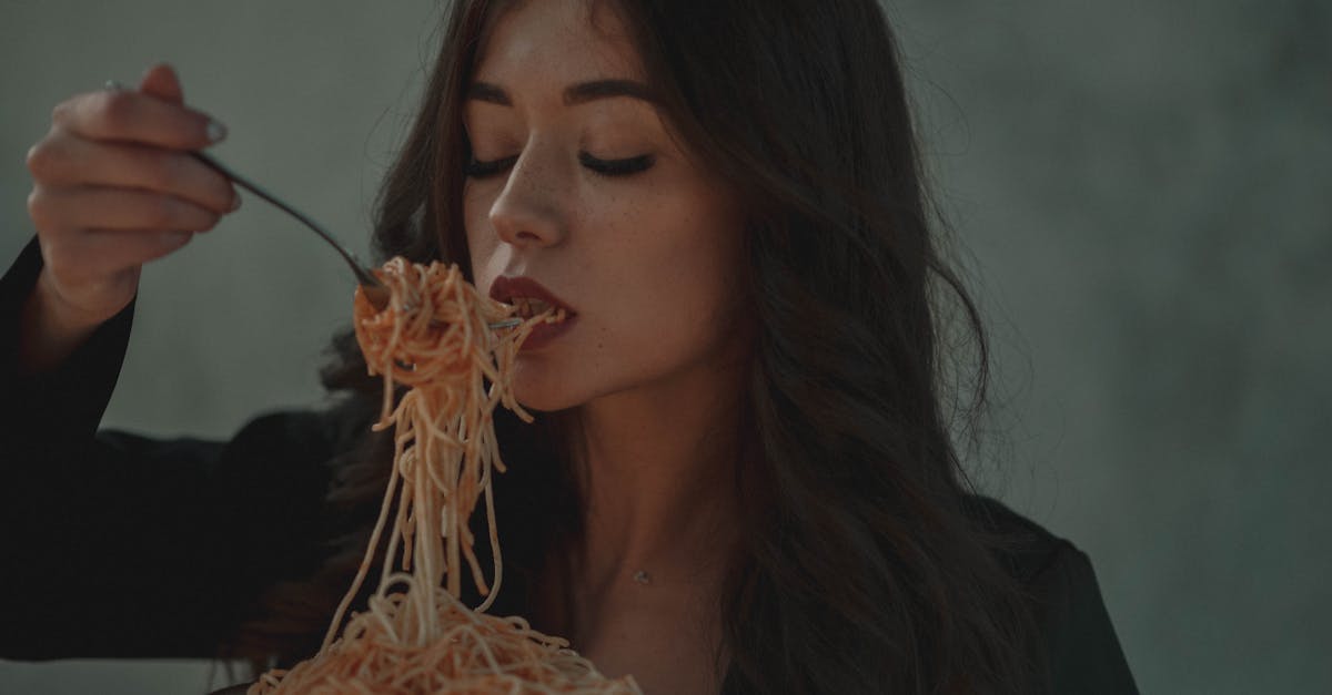 A woman relishes a forkful of spaghetti pasta in a cozy indoor setting, conveying warmth and indulgence.