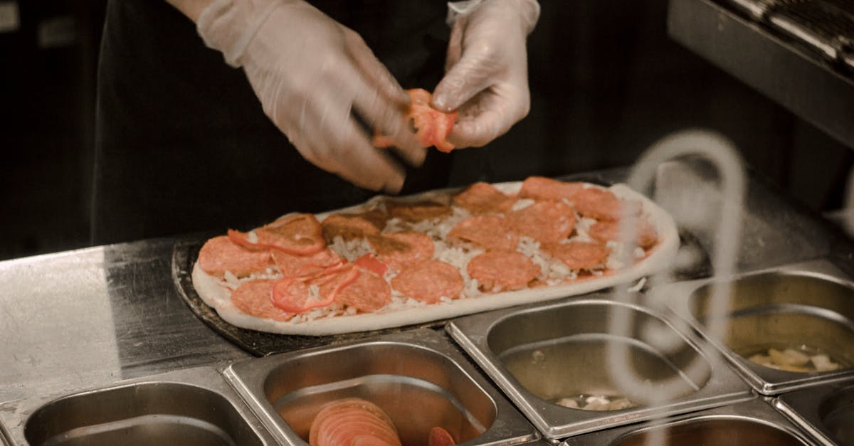 Chef wearing gloves prepares a gourmet pizza with fresh toppings in a professional kitchen.